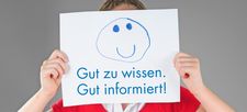 Foto Mädchen hält sich Papier mit Aufschrift "Gut zu wissen. Gut informiert" vors Gesicht
