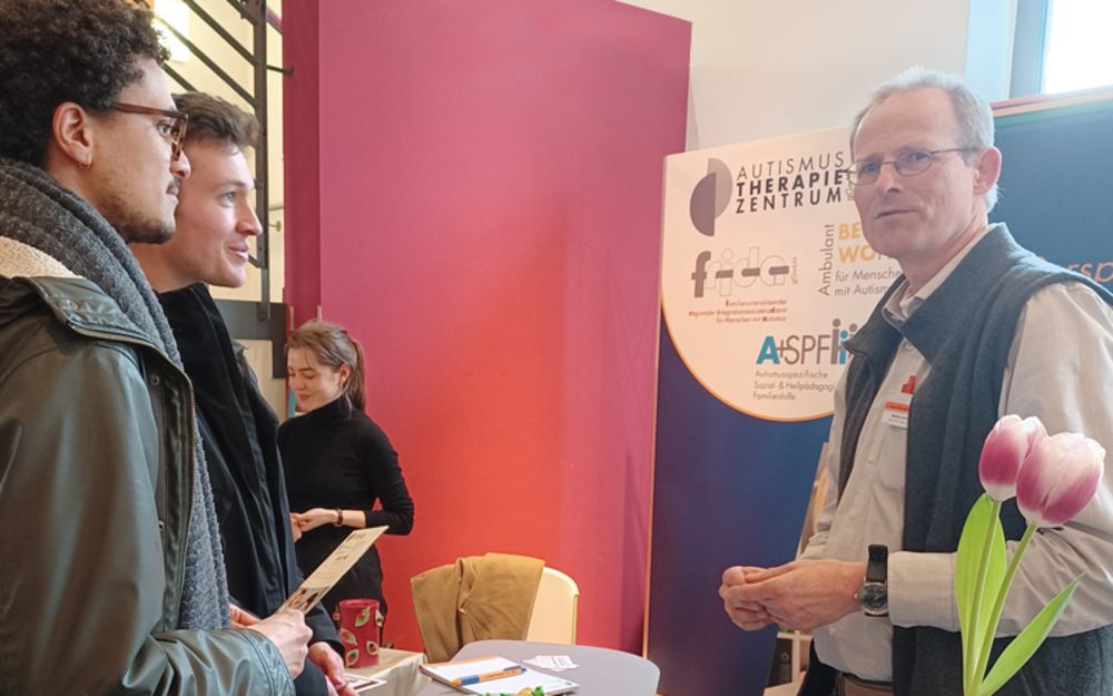 Foto zeigt Mitarbeiter Markus Schneider (FRIDA gGmbH) am Infostand mit zwei Besuchern