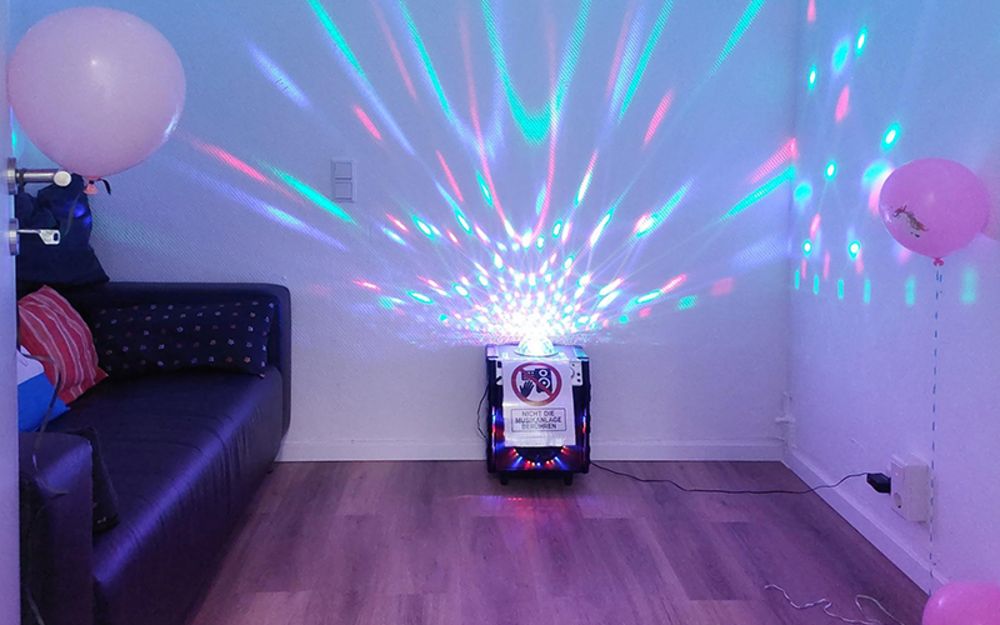 Foto zeigt den Medienraum, in dem links ein Sofa steht. Ein Beamer wirft bunte Strahlen an die Wände.