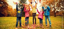 Foto zeigt Kinder auf einer Rasenfläche, die Herbstlaub in die Luft werfen
