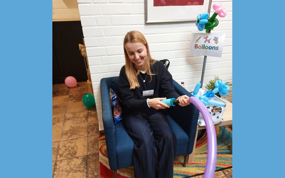 Foto zeigt Mitarbeiterin Lucienne Schmitz, die aus Luftballons Tiere bastelt. Sie sitzt dabei in einem Sessel im Eingangsbereich des ATZ Gütersloh.