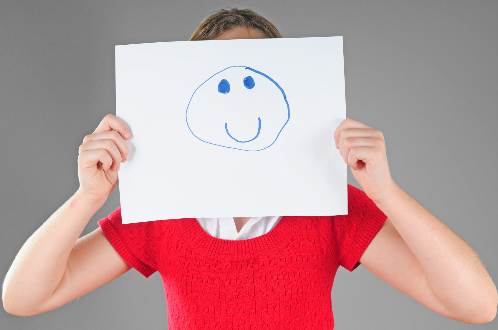Mädchen hält sich Blatt Papier mit Smiley drauf vors Gesicht